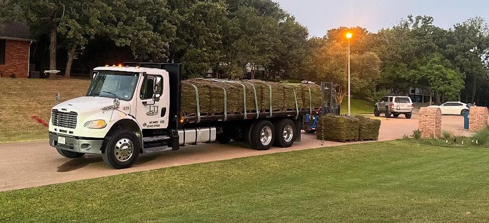 Pallets of fresh-cut sod on a flatbed truck in a Fort Worth driveway at sunrise